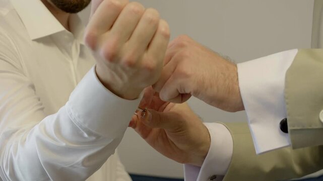 Best man assists the groom with putting on his cufflinks before the wedding ceremony.