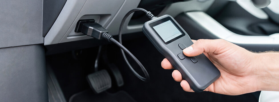 Man holding diagnostic scanner connected to car OBD port. Computer diagnostics and repair of vehicle engine. Automotive mechanic checking error codes with electronic tester. auto service technology