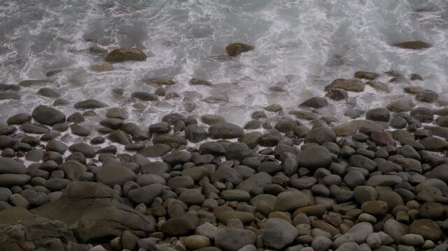 Waves washing over rounded grey boulders on a pebble beach in Higashiizu, Izu, Japan, under an overcast sky, close-up shot