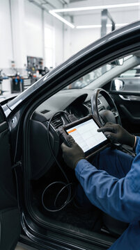 Mechanic using tablet with diagnostic software connected to car computer system. Auto repair service technician performing electronic vehicle diagnostics in modern garage. Automotive technology.