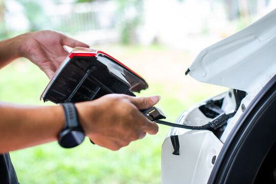 Mechanic hands holding a removed car tail light assembly while disconnecting the electrical cable wiring harness in a repair service shop.