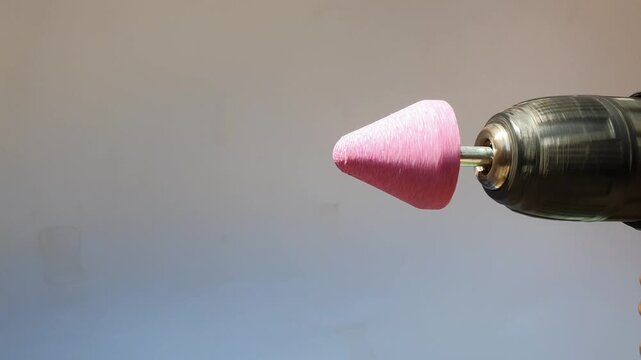 Close up of a pink cone-shaped mounted grinding stone bit attached to a cordless power drill chuck, spinning rapidly against a white background.