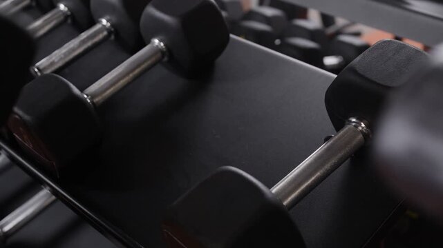 Rack of black rubber hex dumbbells in a gym setting, organized and ready for weight training