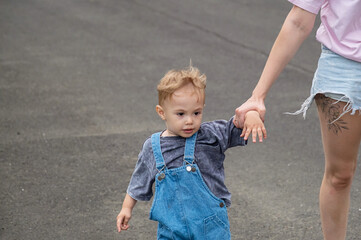 Fototapeta premium Mother pulling stubborn toddler boy by hand on street.