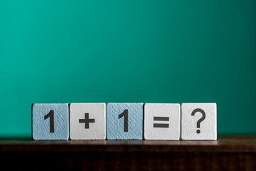 Obraz premium Simple math equation on wooden blocks with question mark, closeup. White and light blue wooden cubes showing the mathematical equation one plus one equals question mark stand against green background