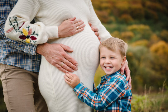 A pregnant woman, man, and their little son standing together on a scenic hill with a forest background, embracing. Photo family closeup in autumn. Family portrait outdoors in autumn.