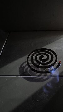 Burning mosquito coil with blue smoke on floor in dark room with dramatic light close up