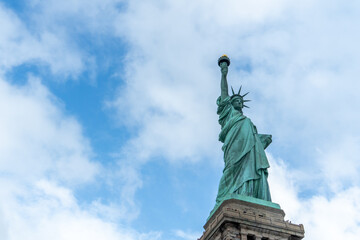 Statue of Liberty rising against a bright blue sky with soft white clouds, capturing freedom, democracy, travel, American heritage, tourism, and an iconic urban landmark in New York City. © byjeng
