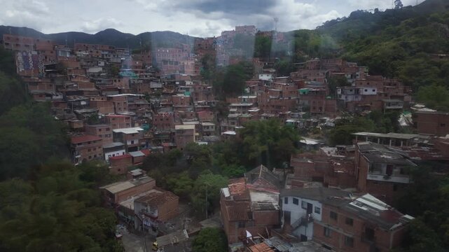 View through a cable car window over a dense hillside neighborhood in Medellin, Colombia, colorful brick houses climbing green mountains, urban transportation concept