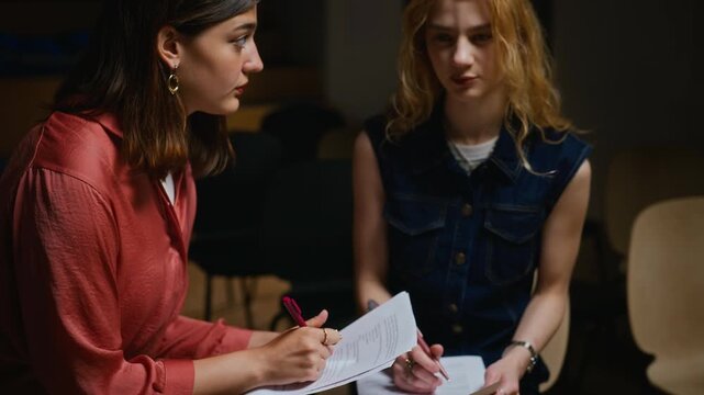 Young Caucasian actresses sitting in auditorium discussing and editing theater script with pens. Video suitable for educational projects and acting school promotions