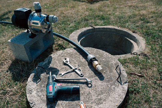 Tools and suction pipe with brass check valve lying on concrete well cover next to surface water pump