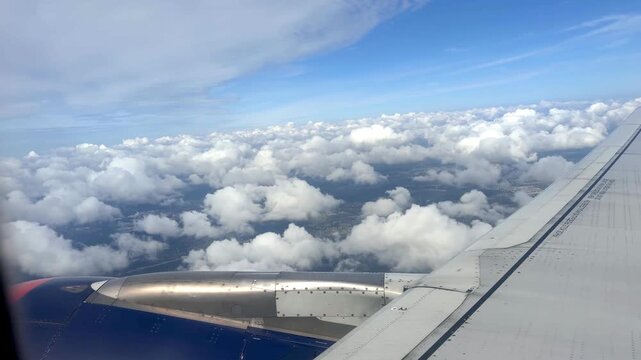 Airplane wing and clouds seen from the window, illustrating the gradual descent through the cloud layer with visible land below