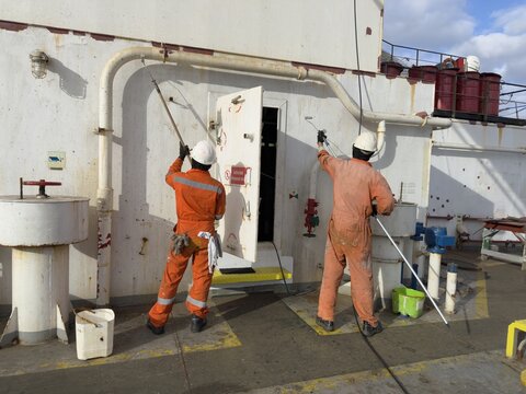 crew members painting aft part of ship superstructure.