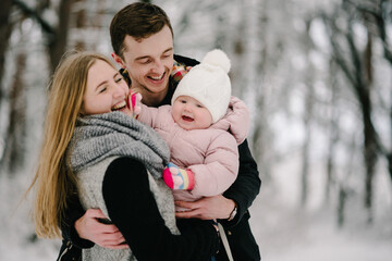 Fototapeta premium Tender family hugs in snowy winter forest, happy mother, father and child smiling. Atmosphere of coziness and family harmony. Closeup.