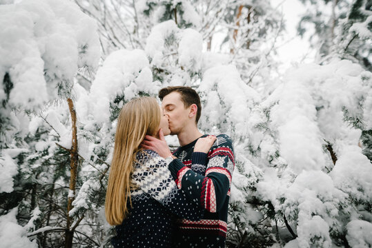 Loving couple hugging, woman and man kissing in the middle of a snowy winter forest. Romantic valentines day. Closeup.