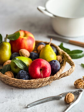 Ein Korb mit &Auml;pfel, Birnen, Zwetschken und Waln&uuml;ssen auf ienem grauen Tisch. Herbst, Obst.