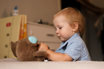 Naklejka premium Toddler boy playing with a stuffed animal on a bed