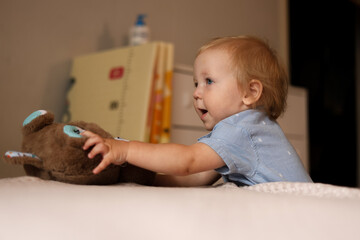 Naklejka premium Curious toddler reaching for a soft teddy bear on a bed