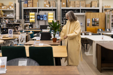 Fototapeta premium Mature woman browsing different dining tables in a large home goods store