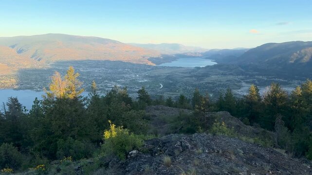 Panoramic static shot of a serene valley with a river, surrounded by mountains and trees at Mount Nkwala, Penticton, captured from a high vantage point with clear, balanced framing and natural ligh...