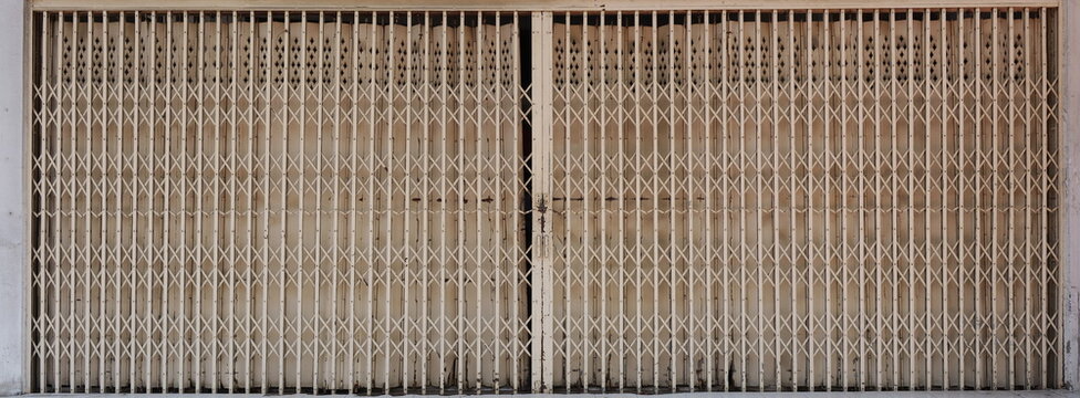 Closed cream-colored metal accordion gate featuring a scissor-lattice pattern over a shoptop entrance