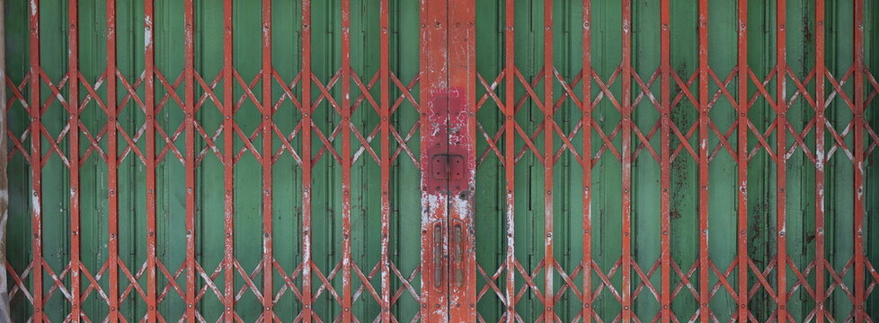 Weathered vintage folding metal gate featuring a red cross-brace lattice over green vertical accordion doors