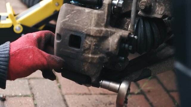 Automotive technician tightening brake caliper bolts with ratchet wrench during vehicle repair. Close up maintenance action with gloved hands fastening caliper hardware on braking assembly. Car