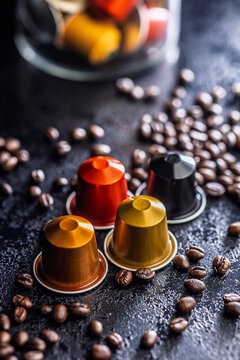 Colorful Coffee Capsules and Espresso Pods Scattered Among Roast Coffee Beans on Dark Surface
