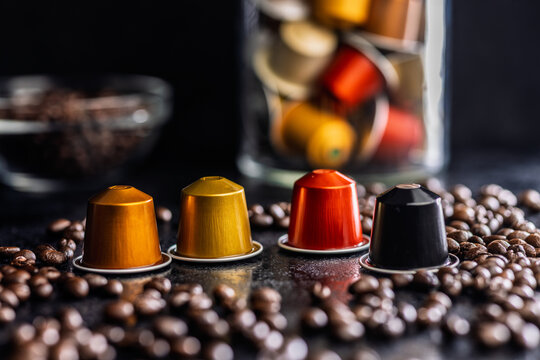 Colorful Coffee Capsules and Espresso Pods Scattered Among Roast Coffee Beans on Dark Surface