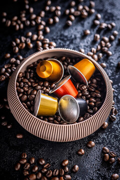 Colorful Coffee Capsules and Espresso Pods Nestled in Bowl of Roasted Coffee Beans on Dark Surface