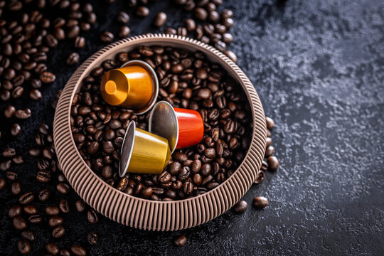 Colorful Coffee Capsules and Espresso Pods Nestled in Bowl of Roasted Coffee Beans on Dark Surface