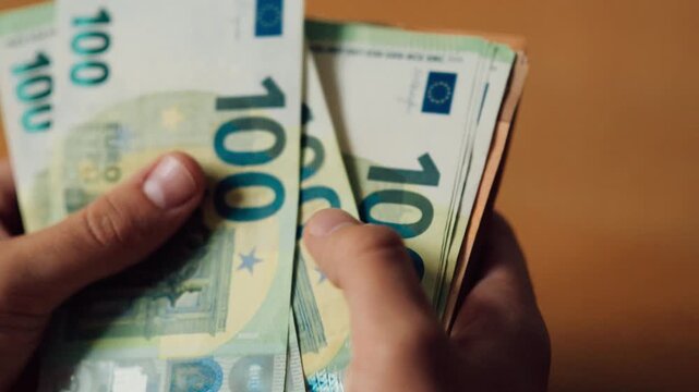 Person counting euros in hands at a table in a bright indoor setting during the day