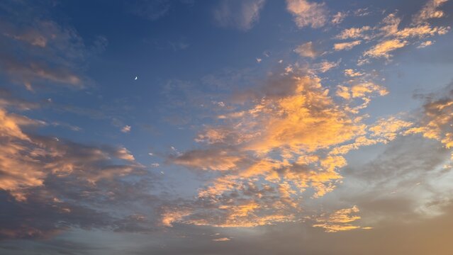 Golden clouds and a crescent moon fill the blue sky