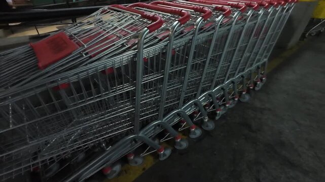 Empty metal shopping carts with red handles standing in a row in a dimly lit underground parking lot
