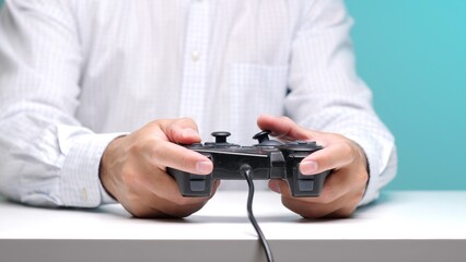 Hands of a person actively gripping a wired video game controller, engaging in digital recreation and entertainment against a blue background, symbolizing leisure activity © Aliaksandr
