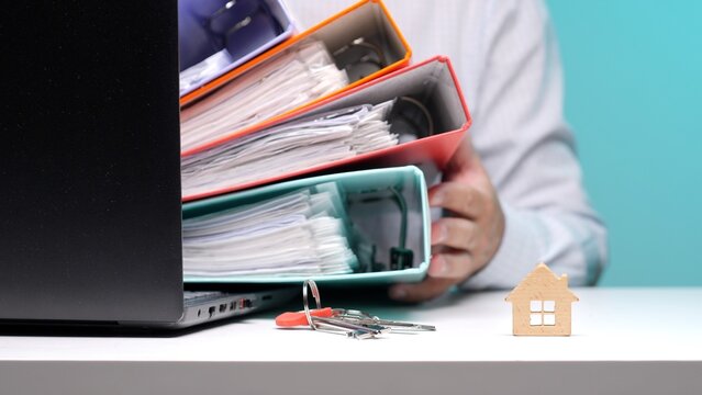 Hands holding a heavy stack of file folders and documents representing the paperwork, bureaucracy and financial burden of mortgage applications, property purchase and home ownership