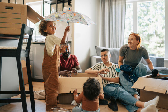 Happy boy playing with umbrella while family sitting in living room during relocation