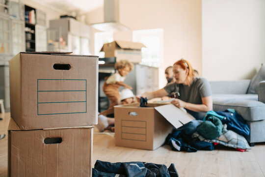 Cardboard boxes stacked on each other while family unpacking goods in background