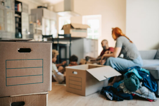Stack of cardboard boxes with family sitting in background during house relocation