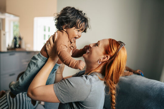 Side view of redhead woman playing with her happy toddler in new apartment