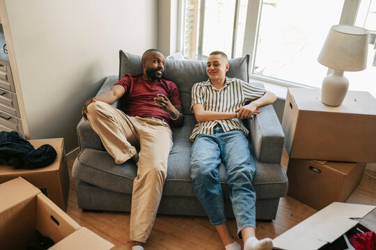 High angle view of father and son resting on sofa surrounded by boxes during house relocation