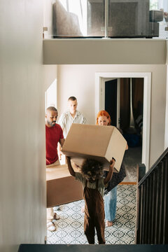 Boy carrying cardboard box with his parents on moving day