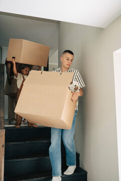 Boy carrying large cardboard box while moving down on stairs during house relocation