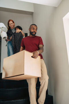 Man carrying large cardboard box while moving down on stairs in new apartment
