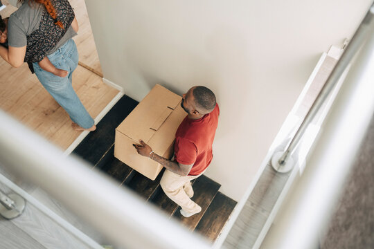 High angle view of man carrying moving box while moving up on steps in new home