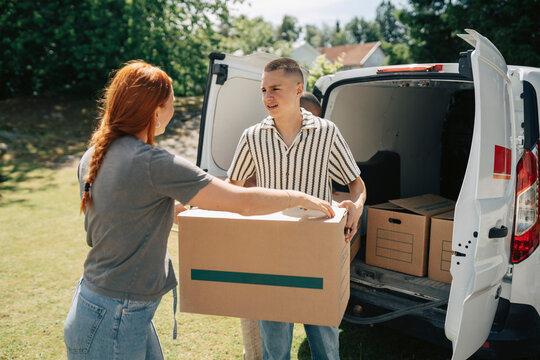 Son passing cardboard box to her mother while standing by white van on moving day