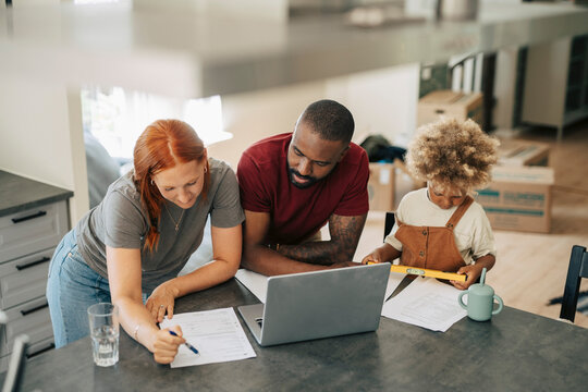 Diverse parents using laptop and checking paperwork for during house relocation