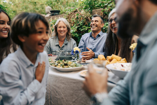 Cheerful family members enjoying sunny afternoon meal while sitting in back yard