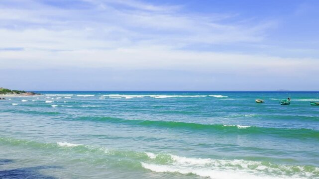Cool waves roll on the shore in Mui Ne, Lam Dong. Small boats move across the water under a clear sky. Enjoy this view of the ocean and the boats in the distance during the day.