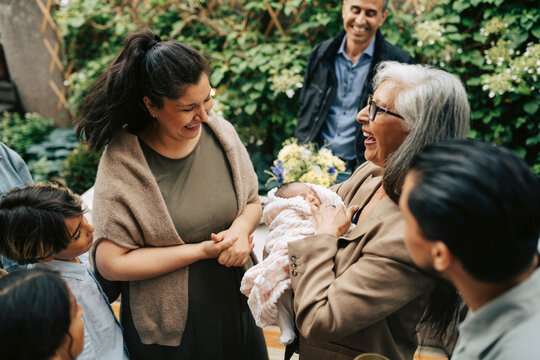 Multi-generational family laughing together around newborn baby in back yard